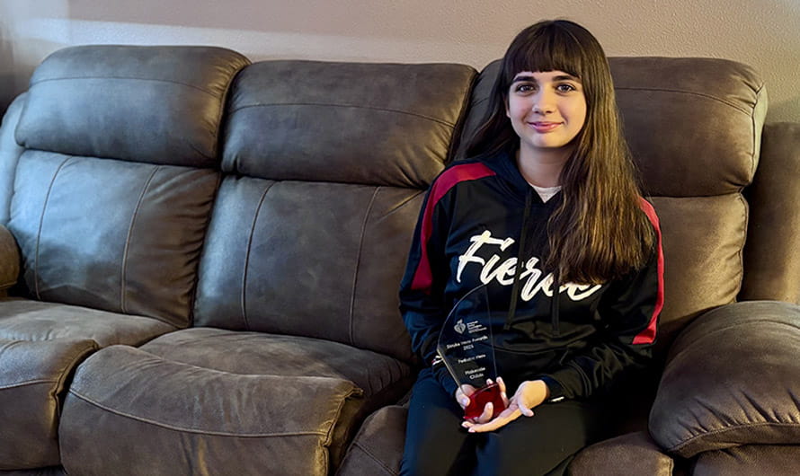 Makenzie Childs is sitting on a sofa holding her Pediatric Stroke Hero Award trophy. Makenzie Childs is sitting on a sofa holding her Pediatric Stroke Hero Award trophy.