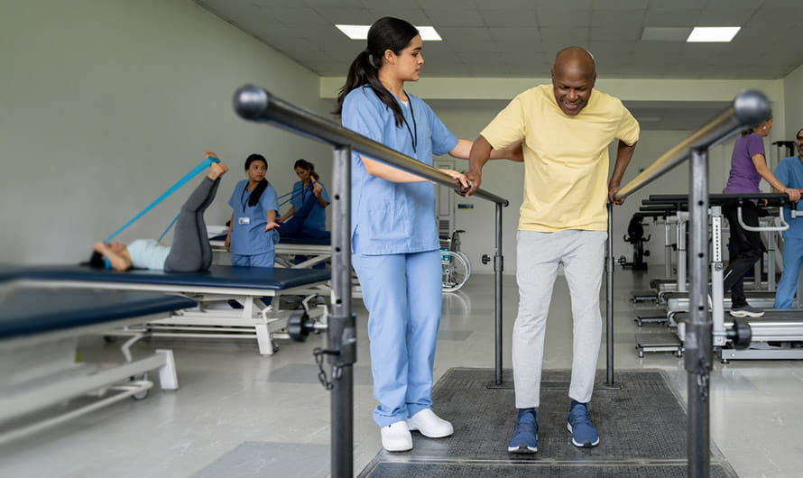 A young woman healthcare professional is helping an older man walk in a rehab facility.