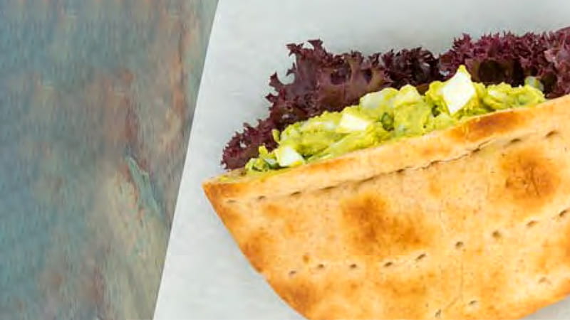 A pita pocket filled with egg avocado salad and lettuce is arranged on a plate. A pita pocket filled with egg avocado salad and lettuce is arranged on a plate.
