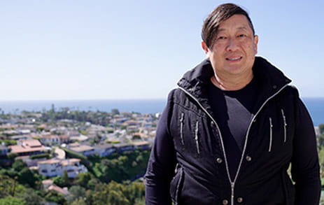 Stroke survivor, Dave, is smiling on an overlook with a neighborhood and the ocean in the distance behind him.