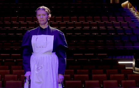 Stroke survivor, Maggie, is standing on a stage in costume with theatre seats in the background.