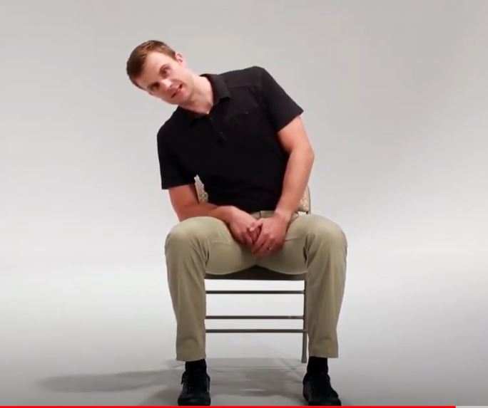 A White man is sitting in a chair leaning his head and upper body over to his right.