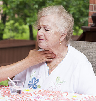 A caregiver has her hand on a senior woman's throat to assist with swallowing.