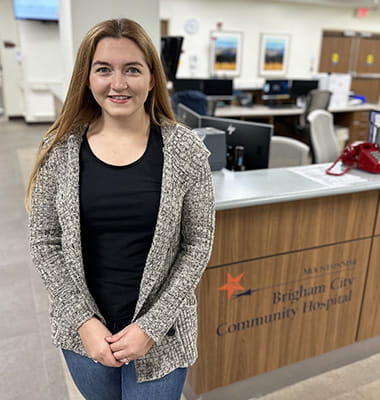 Whitney Sheffield is standing in front of the nurse's station at Brigham City Community Hospital (photo credit: HCA Healthcare)