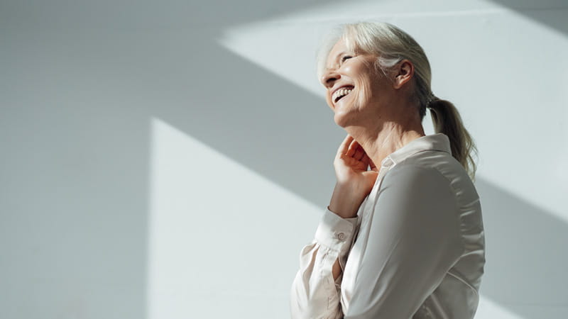 Una vista de perfil de una mujer adulta mayor sonriente con una fuerte luz.