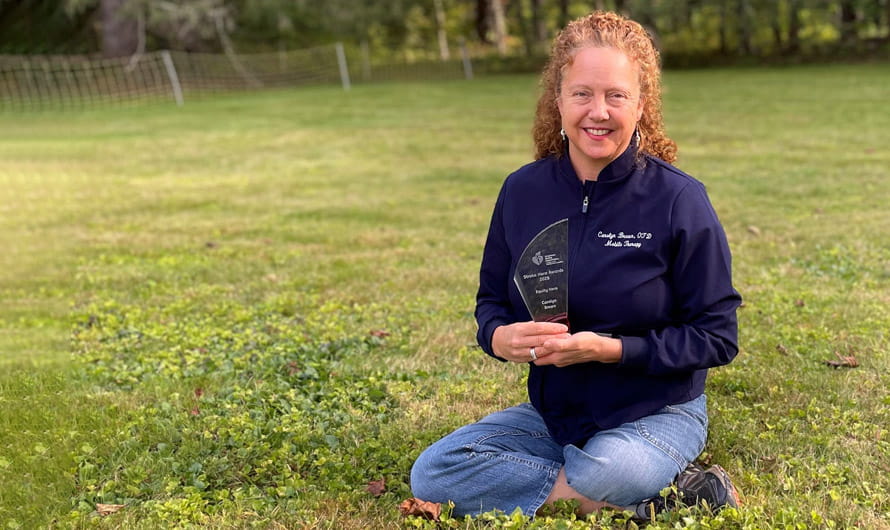 Carolyn Brown is sitting outside in the grass holding her Stroke Hero Award trophy. Carolyn Brown is sitting outside in the grass holding her Stroke Hero Award trophy.