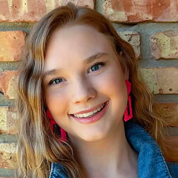 A close-up of Lexi Frederick smiling against a brick background.