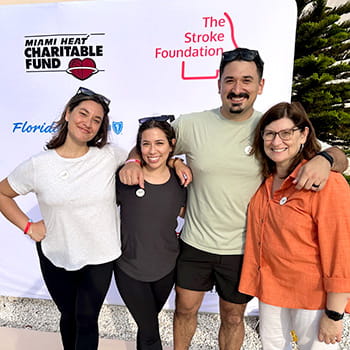 Four people are posing in front of a step-and-repeat showcasing The Stroke Foundation logo.