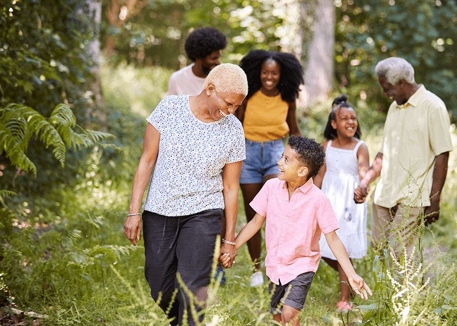 A senior Black woman and man are walking with their multigenerational family along a nature trail through trees. A senior Black woman and man are walking with their multigenerational family along a nature trail through trees.