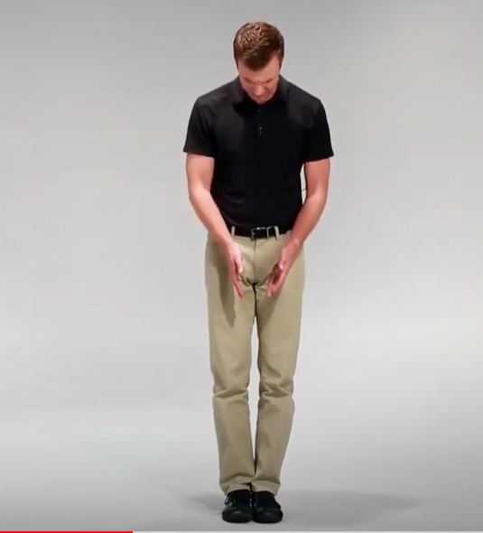 A White man is standing up straight and looking down with- his feet together.