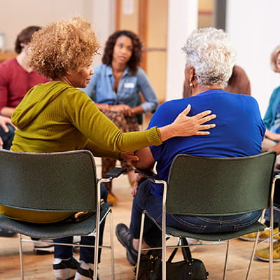 A woman is comforting another woman in a support group circle.