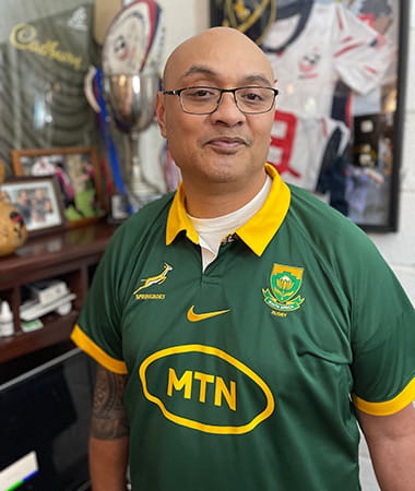 Silivenusi “Nusi” Tukuafu, un sobreviviente de un derrame cerebral, está parado frente a recuerdos deportivos vistiendo una camiseta de rugby de los Springboks.